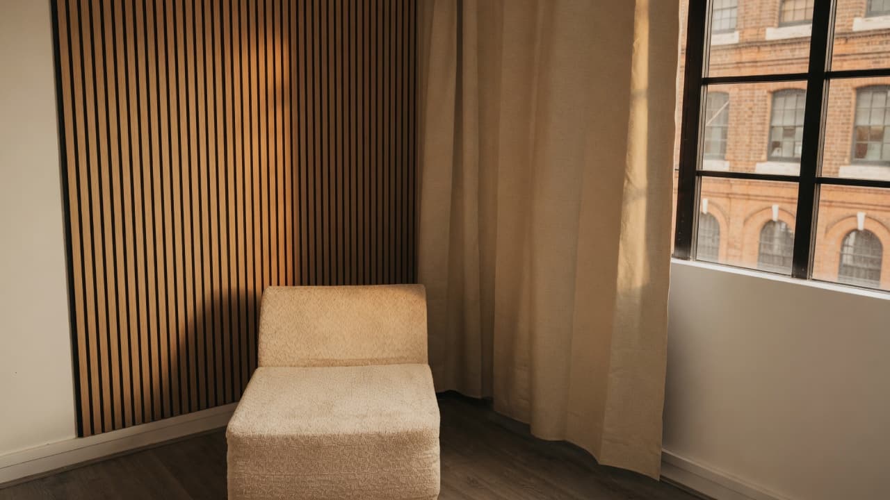 The Content Suite interview nook: oak slat wall, cream chair, linen curtain and warehouse windows