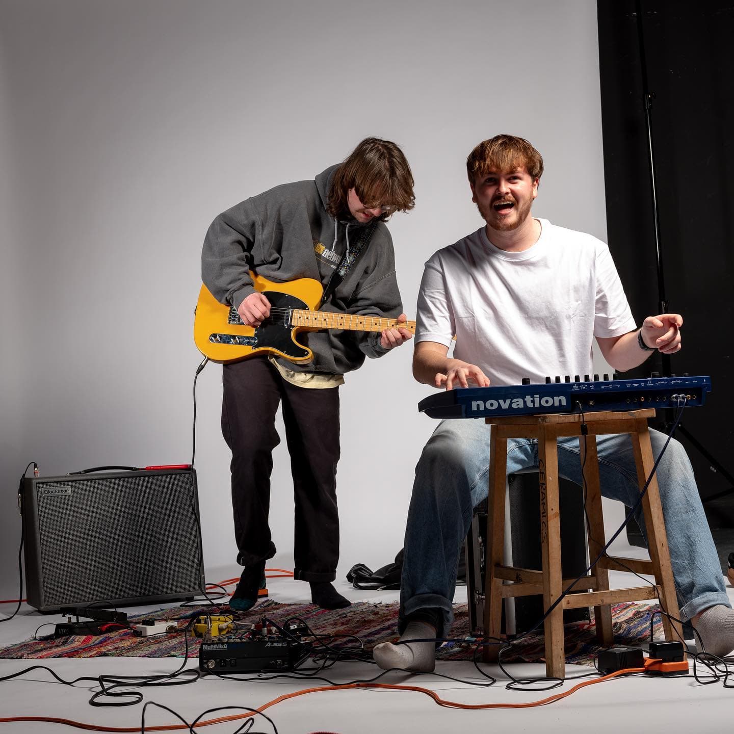 Live session — guitarist and keyboardist performing against a grey backdrop