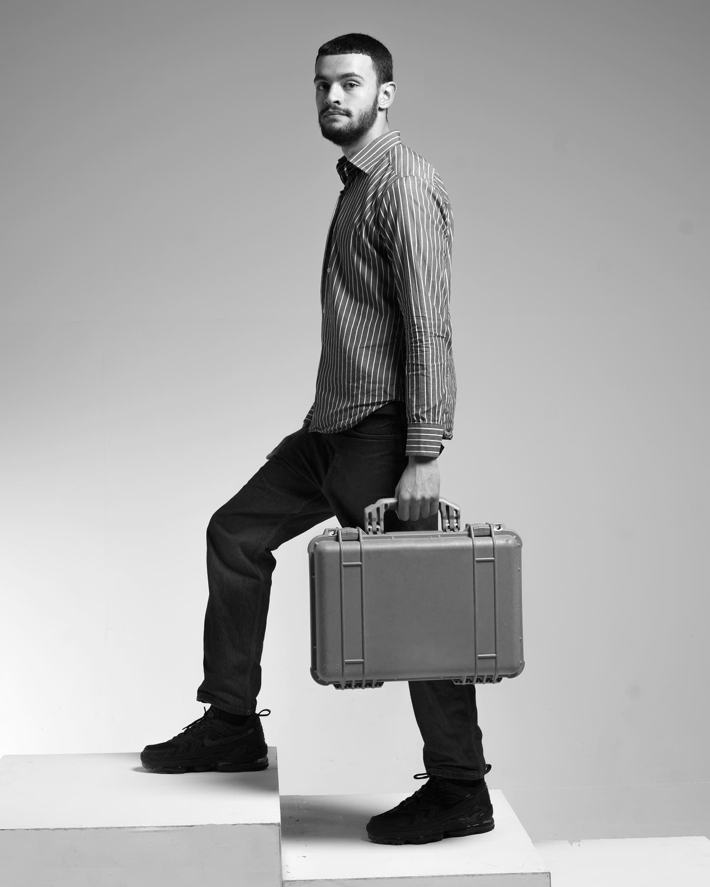 Black-and-white studio portrait: man stepping up holding a hard equipment case