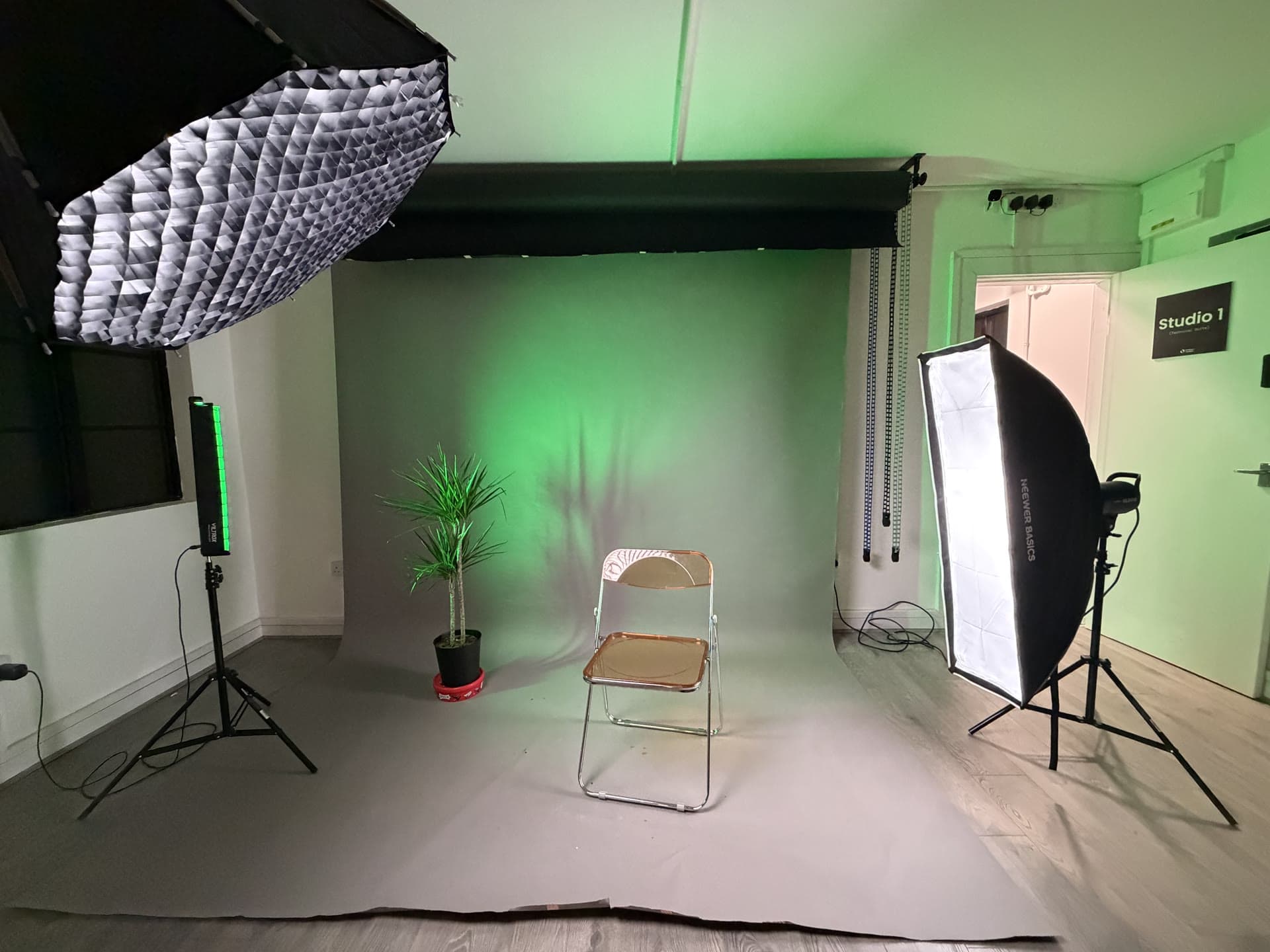 Studio One: grey seamless backdrop with a folding chair, plant, octabox and strip light, Studio 1 door sign